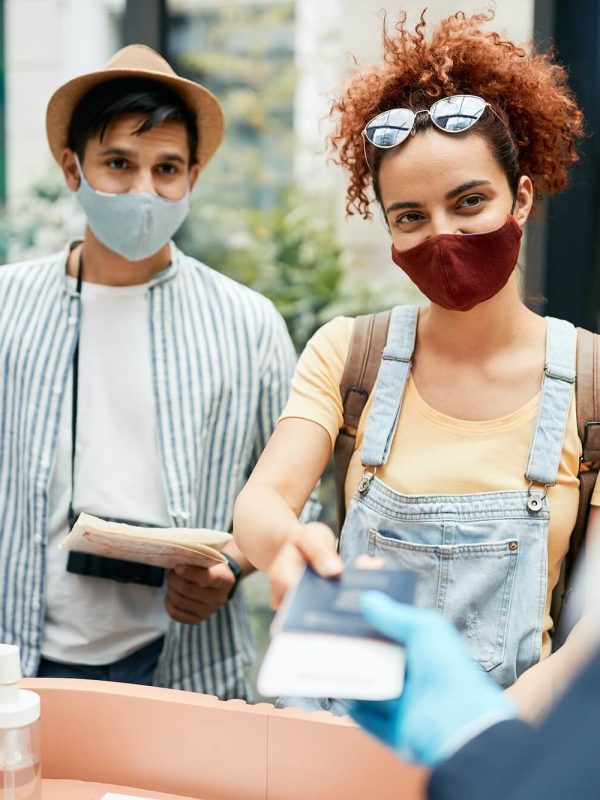 young traveling couple wearing protective face mask during check in at hotel reception 1 1.jpg